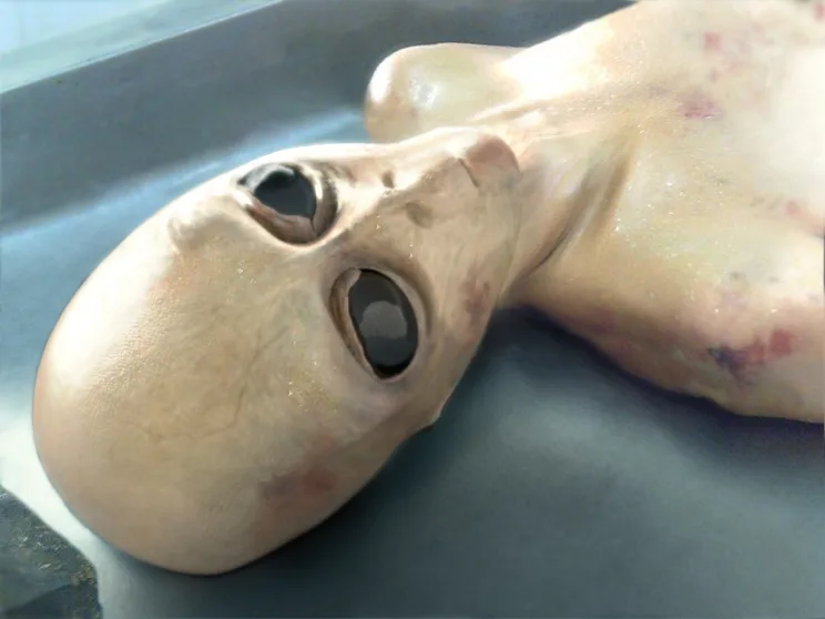 Close-up of a pale alien body with large black eyes on an examination surface